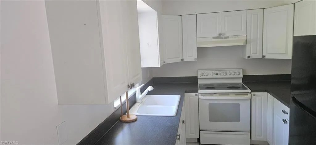 Kitchen featuring black refrigerator, sink, white cabinetry, and white range with electric stovetop