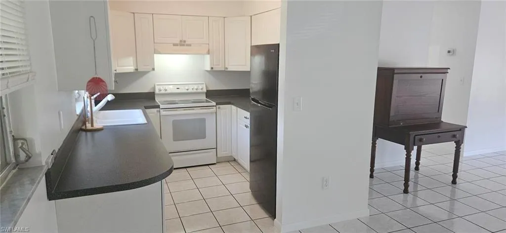 Kitchen with white cabinets, light tile patterned flooring, sink, and white electric range oven