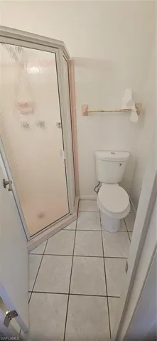 Bathroom featuring toilet, a shower with door, and tile patterned flooring