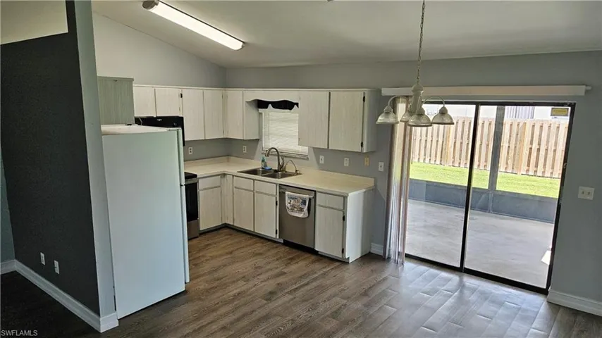 Kitchen featuring light countertops, appliances with stainless steel finishes, lofted ceiling, dark wood-type flooring, and hanging light fixtures