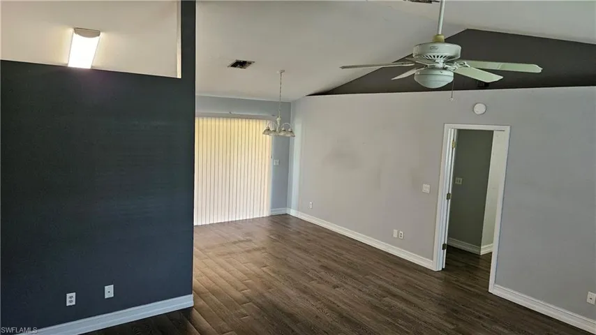 Empty room featuring lofted ceiling, dark wood-type flooring, a chandelier, and ceiling fan