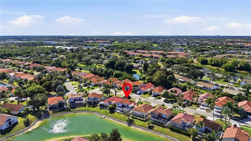 Suburban neighborhood featuring a community lake with a fountain, mature trees, and a collection of properties with tile roofs