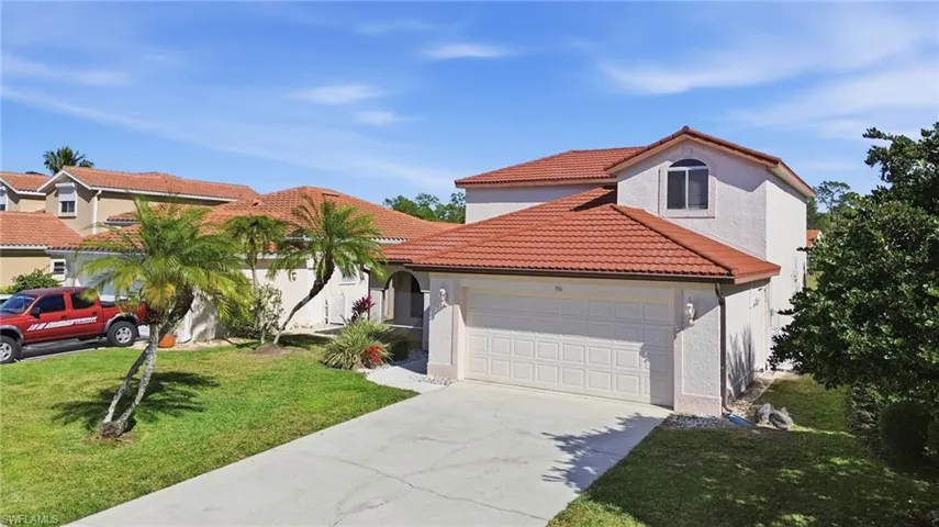 Mediterranean-inspired architecture featuring a terracotta tile roof, stucco exterior, attached two-car garage, concrete driveway, and mature palm trees