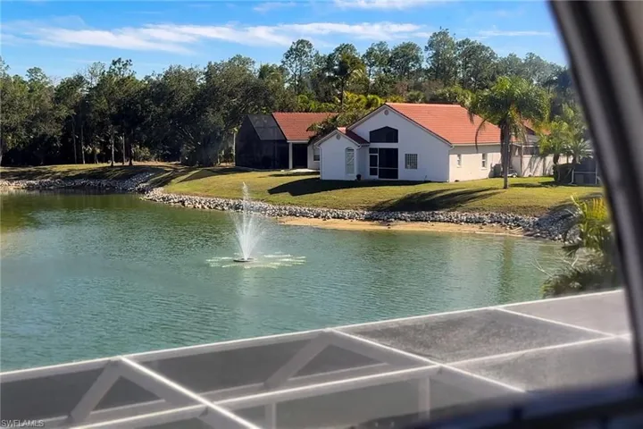 Waterfront property featuring a fountain, rock-lined shore, lush green lawn, and mature trees
