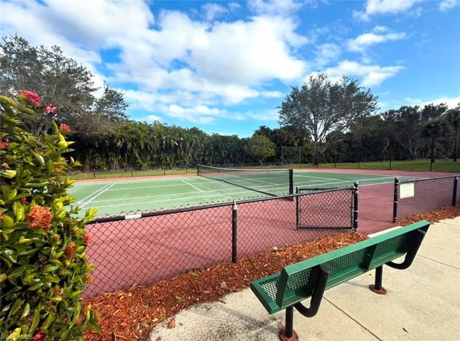 Tennis court featuring a green playing surface, red perimeter, black chain-link fencing, and surrounding mature trees