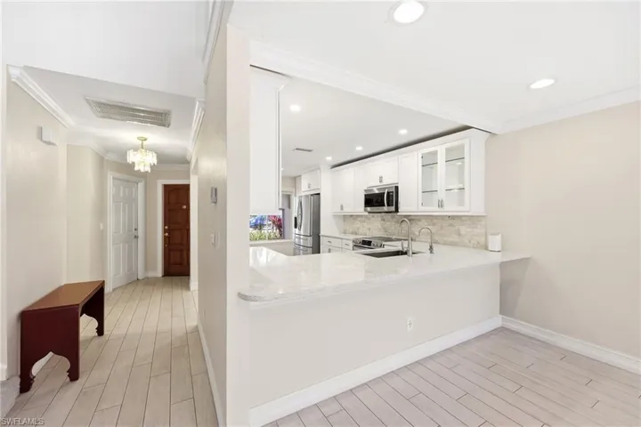 Open concept kitchen with white cabinetry, stainless steel appliances, light-toned countertops, and a stone-tile backsplash