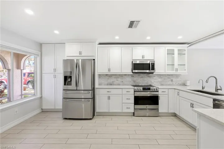 White shaker cabinetry with brushed nickel hardware, stainless steel appliances, light-toned tile flooring, light-colored countertops, and a subway tile backsplash