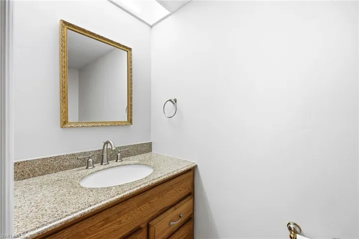Vanity area featuring a granite-style countertop, undermount sink with brushed nickel faucet, wood-finish cabinetry, and an ornate framed mirror