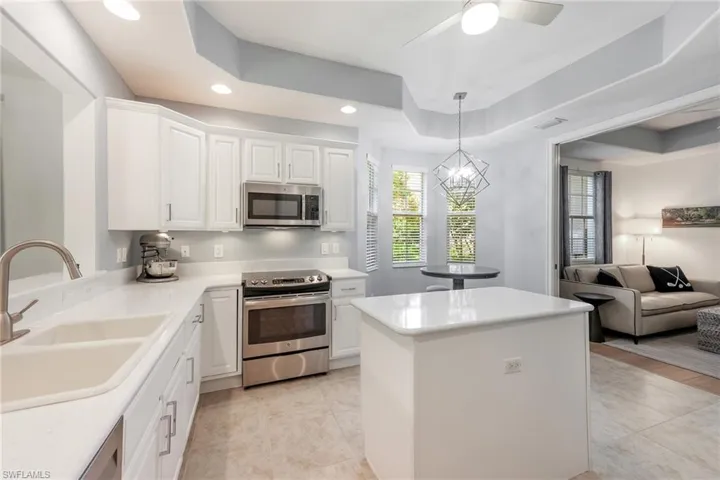 Kitchen with a raised ceiling, sink, hanging light fixtures, white cabinetry, and stainless steel appliances