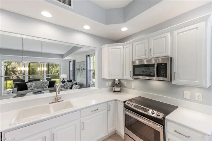 Kitchen featuring stainless steel appliances, a raised ceiling, sink, an inviting chandelier, and white cabinetry