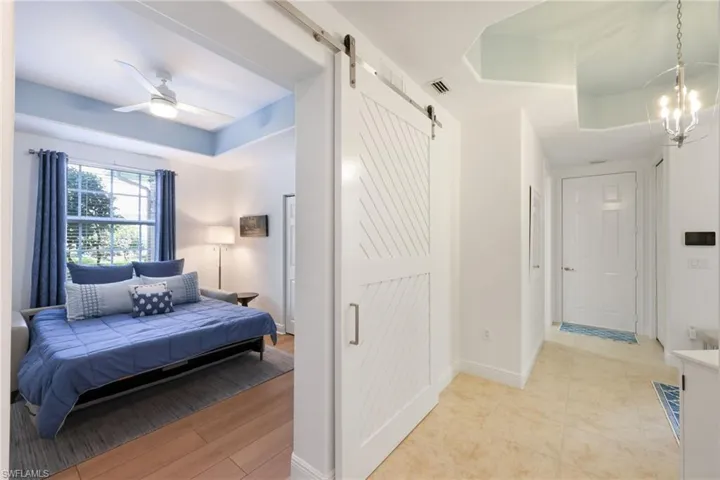 Bedroom/Den with a barn door, a tray ceiling, ceiling fan and wood-style floors