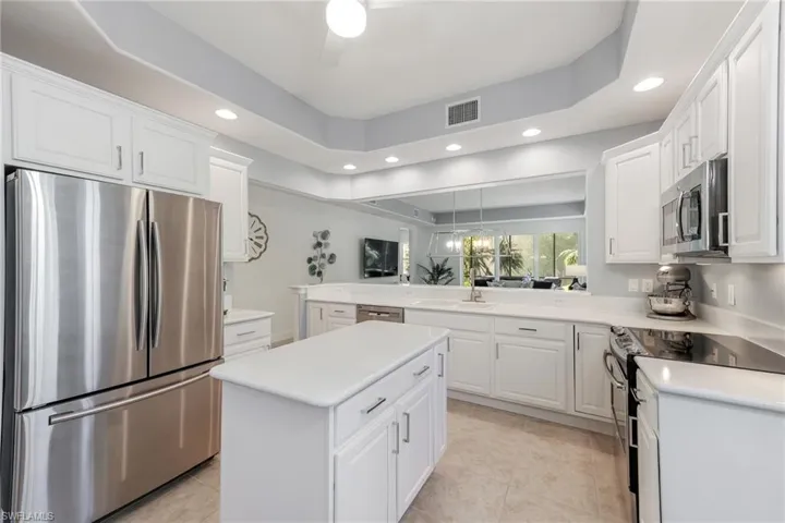 Kitchen with kitchen peninsula, stainless steel appliances, a kitchen island, light tile patterned floors, and white cabinetry