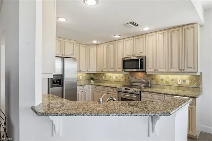 Kitchen featuring cream cabinets, stainless steel appliances, light stone countertops, a kitchen bar, and recessed lighting