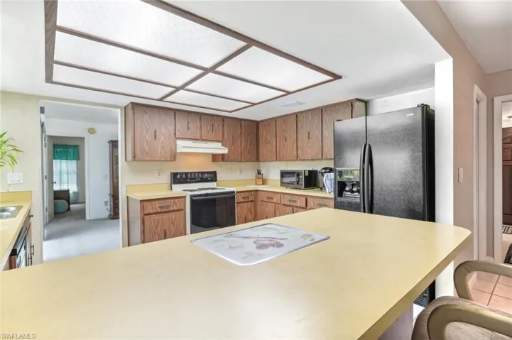 Kitchen with black fridge, white electric range, and light colored carpet