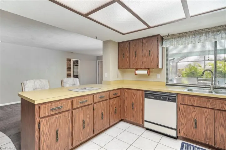 Kitchen with sink, dishwasher, kitchen peninsula, and light tile floors