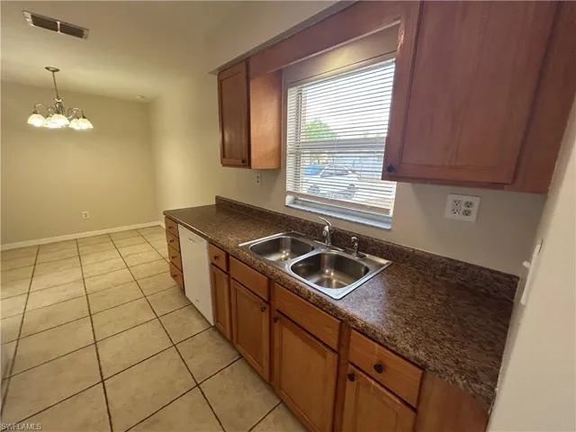 Kitchen with dark countertops, a chandelier, light tile patterned flooring, dishwasher, and wood finish cabinets