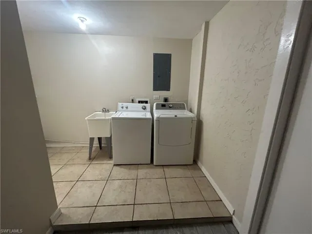 Laundry room featuring washing machine and clothes dryer, electric panel, light tile patterned flooring, and a textured wall