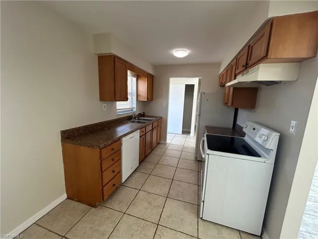 Kitchen featuring white appliances, wood finish cabinets, and dark countertops