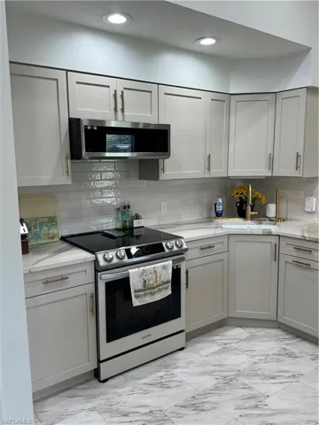 Kitchen with light stone counters, sink, decorative backsplash, stainless steel appliances, and gray cabinetry