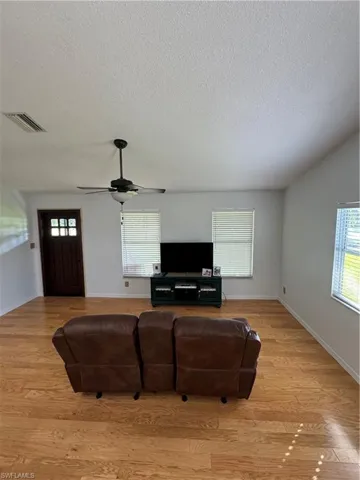 Living room with ceiling fan, a textured ceiling, and light wood-type flooring