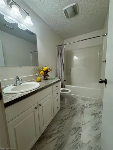 Full bathroom featuring shower / bath combination with curtain, a textured ceiling, vanity, and toilet