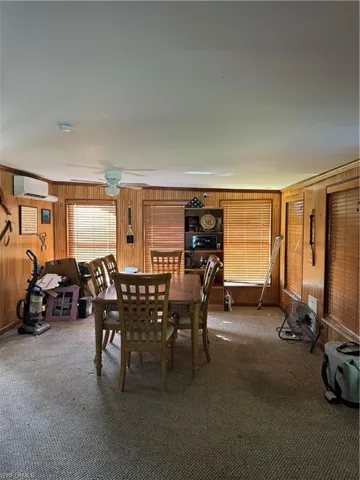 Dining space with wooden walls, a wall unit AC, carpet floors, and ceiling fan