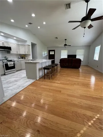 Living room with light hardwood / wood-style floors, vaulted ceiling, and ceiling fan