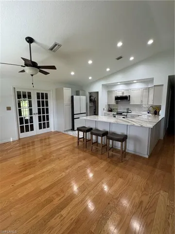 Kitchen featuring a breakfast bar, light wood-type flooring, vaulted ceiling, kitchen peninsula, and white fridge
