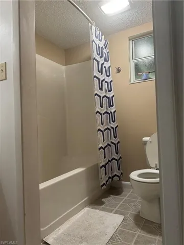 Bathroom featuring a textured ceiling, tile patterned flooring, toilet, and shower / bath combo with shower curtain