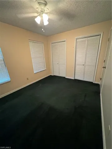 Unfurnished bedroom featuring ceiling fan, a textured ceiling, two closets, and dark colored carpet