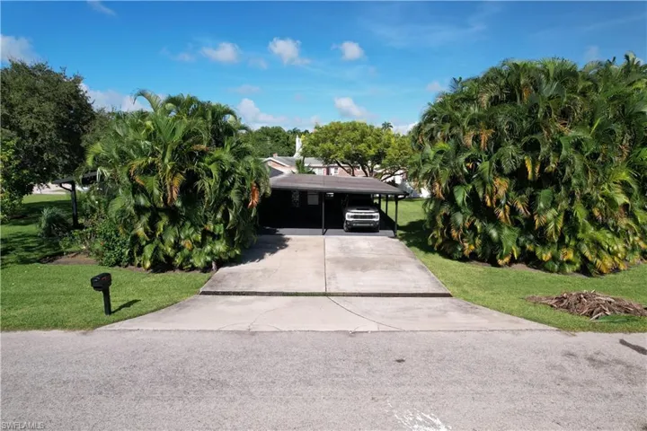 View of property hidden behind natural elements featuring a front yard and a carport