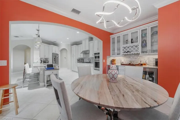 Dining area with arched walkways, a chandelier, crown molding, light tile patterned floors, and bar area