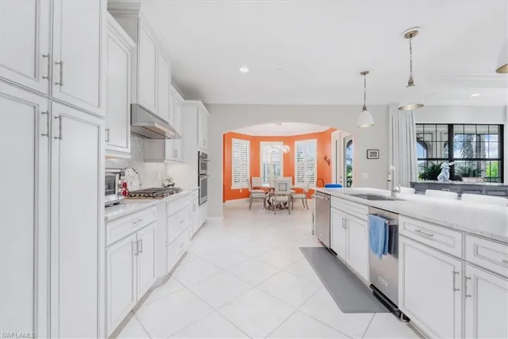 Kitchen featuring arched walkways, white cabinetry, tasteful backsplash, hanging light fixtures, and light tile patterned floors