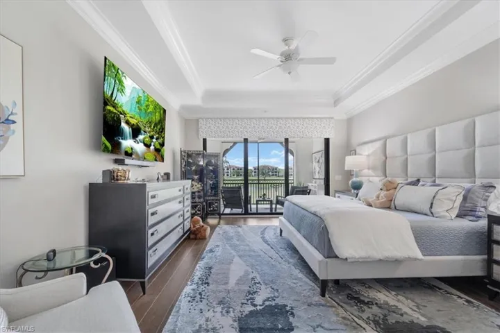 Bedroom with access to outside, a tray ceiling, dark wood-style floors, ornamental molding, and ceiling fan