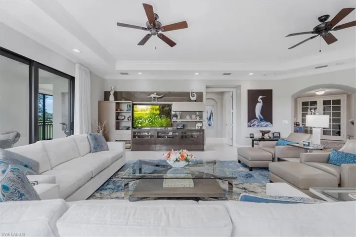 Living area with a raised ceiling, ceiling fan, arched walkways, ornamental molding, and recessed lighting
