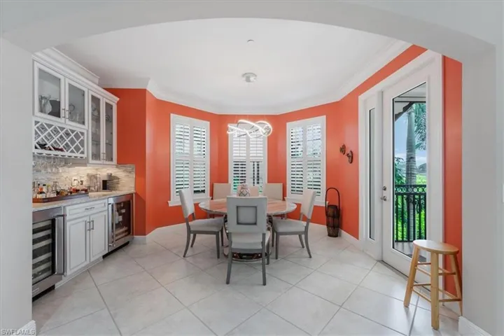 Dining space featuring a bar, a chandelier, wine cooler, ornamental molding, and light tile patterned flooring