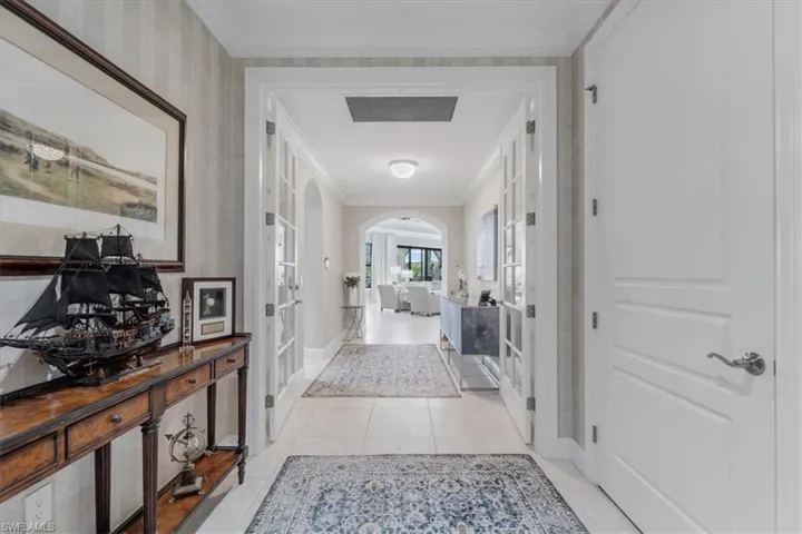 Hallway featuring french doors, arched walkways, ornamental molding, and light tile patterned flooring