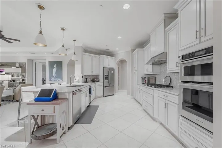 Kitchen with arched walkways, appliances with stainless steel finishes, decorative backsplash, open floor plan, and ornamental molding
