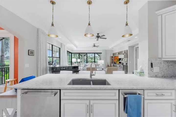Kitchen featuring dishwasher, ceiling fan, white cabinetry, a tray ceiling, and crown molding