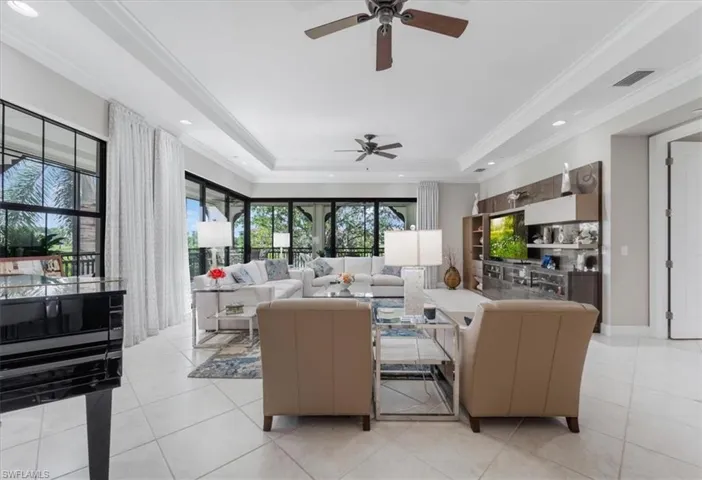 Living area featuring ceiling fan, a tray ceiling, light tile patterned floors, ornamental molding, and recessed lighting
