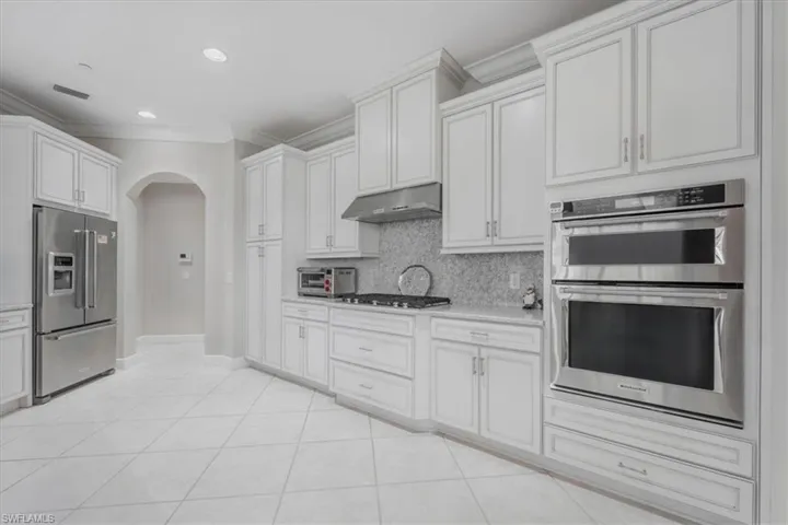 Kitchen with stainless steel appliances, arched walkways, crown molding, tasteful backsplash, and light tile patterned floors