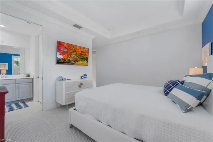 Bedroom with light colored carpet, a tray ceiling, crown molding, and connected bathroom