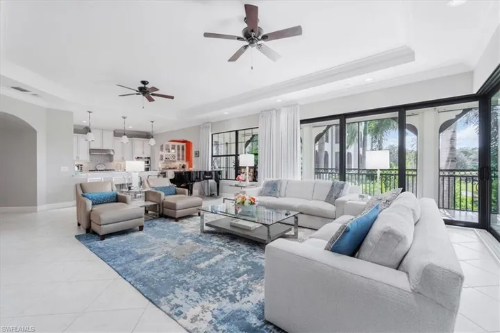 Living area featuring a tray ceiling, arched walkways, plenty of natural light, light tile patterned floors, and crown molding