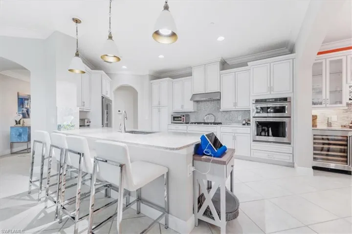 Kitchen featuring arched walkways, ornamental molding, wine cooler, a kitchen bar, and recessed lighting