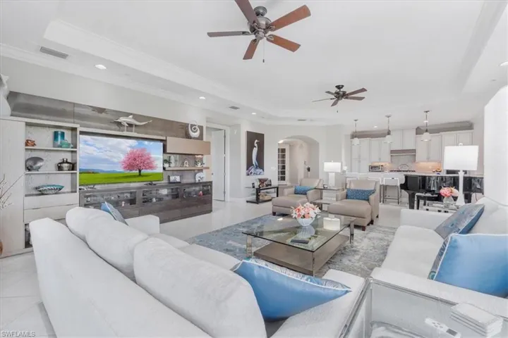 Living room with a raised ceiling, a ceiling fan, arched walkways, ornamental molding, and recessed lighting