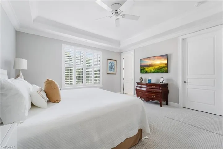 Bedroom with light colored carpet, a raised ceiling, ornamental molding, and a ceiling fan