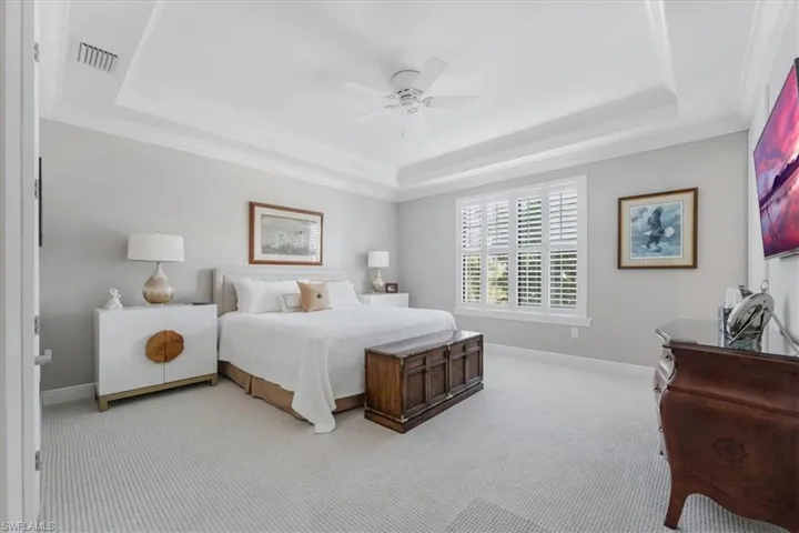 Bedroom featuring a tray ceiling, light carpet, ornamental molding, and a ceiling fan