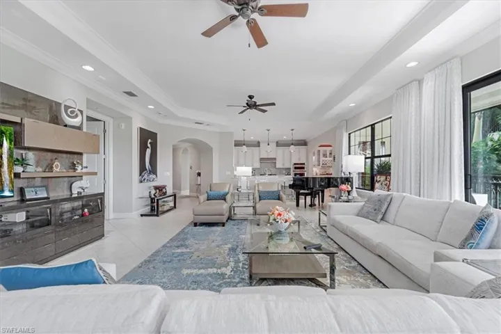 Living room featuring ceiling fan, a tray ceiling, arched walkways, light tile patterned flooring, and ornamental molding