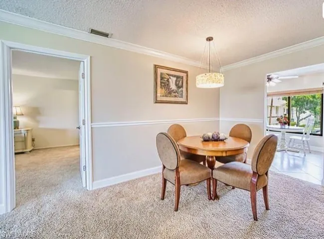 Dining area featuring a textured ceiling, crown molding, ceiling fan, and light carpet