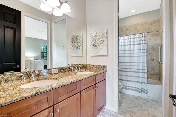 Full bathroom featuring dual vanity, shower / bathtub combination with curtain, toilet, and tile patterned floors
